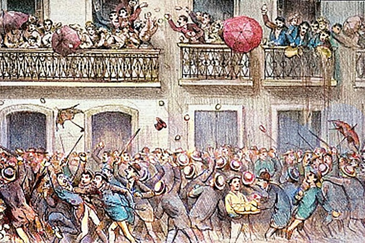 Image of Rua Do Ouvidor during the celebration of Entrudo. Revelers in the street are throwing at each other wax lemons filled with water, and partiers in the balcony are throwing water buckets at the crowd. The mood is festive and chaotic. 